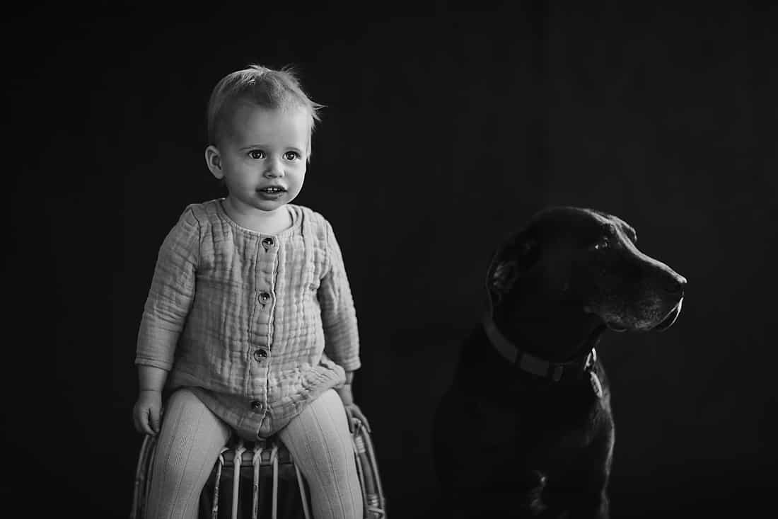 A black and white photograph of child and dog in a studio. Photographed by Shan Radford